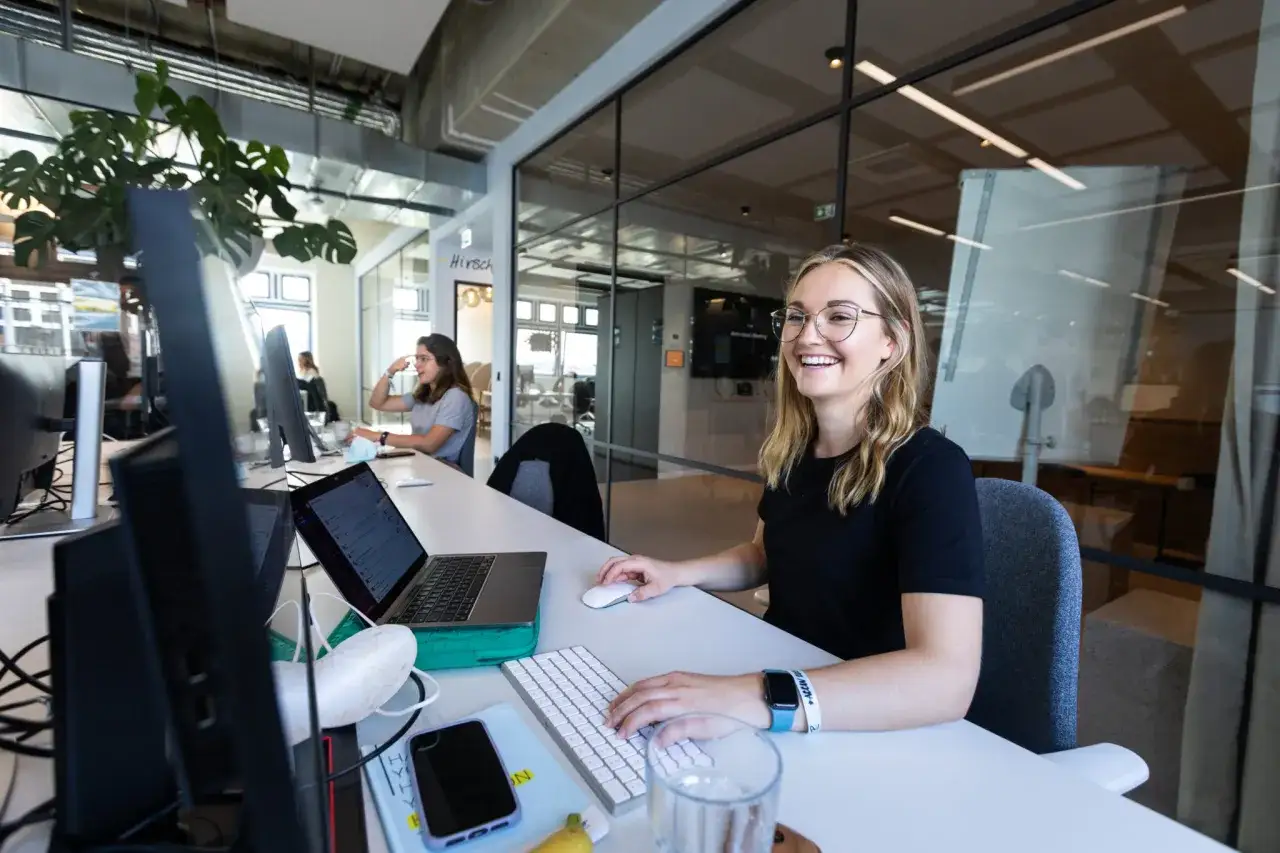 Joven sonr&iacute;e mientras completa una encuesta de satisfacci&oacute;n laboral en su escritorio.