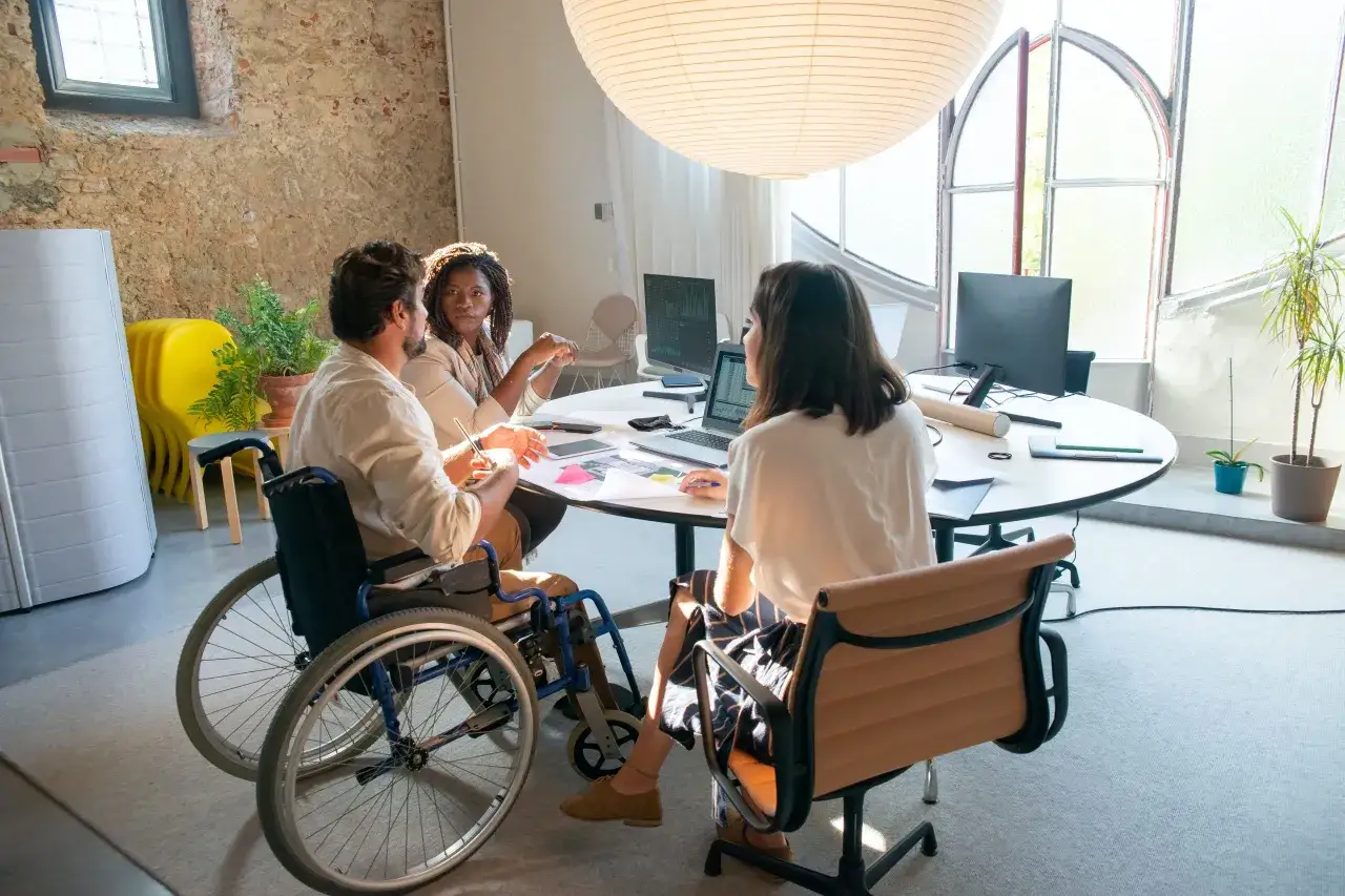 Equipo diverso colabora en un proyecto. Un hombre en silla de ruedas participa activamente, demostrando que el grado de discapacidad no limita el trabajo.