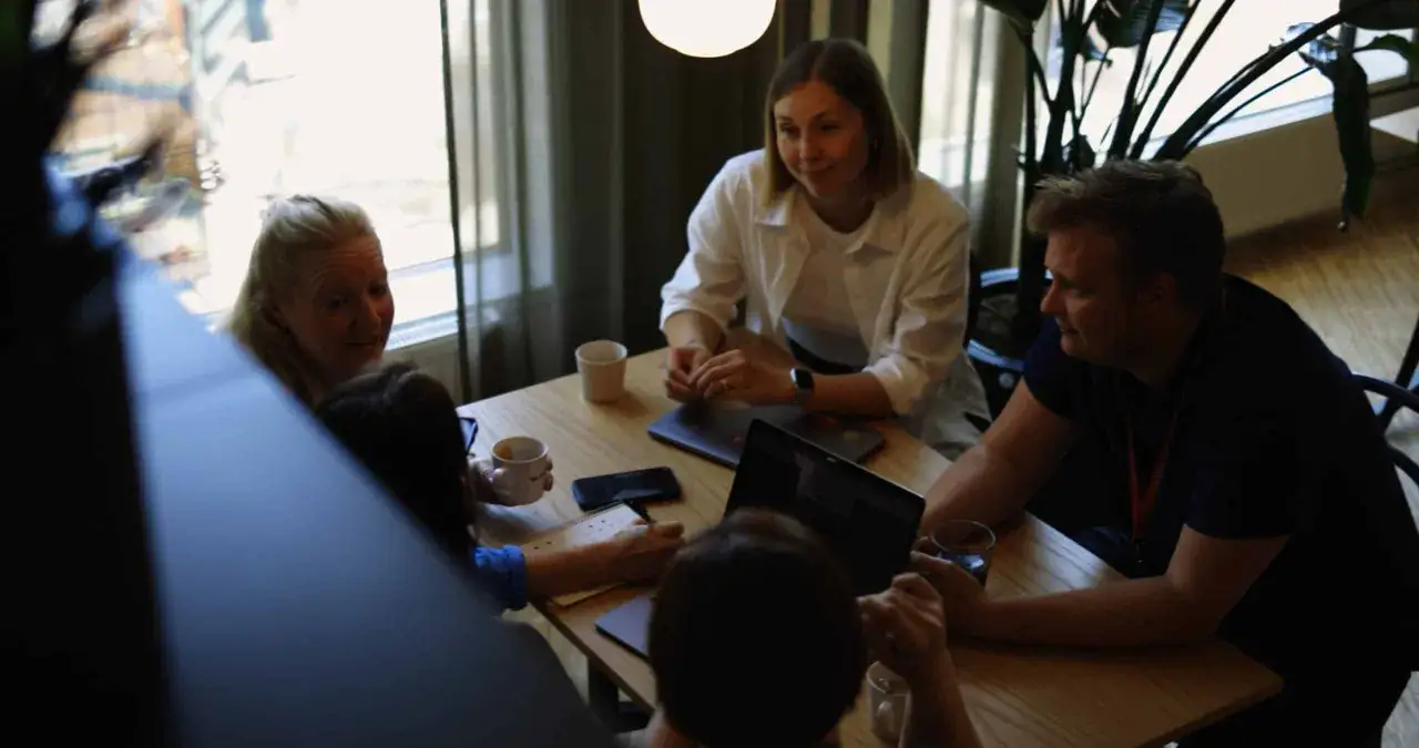 Equipo colaborando en una mesa, con portátiles y tazas. La flexibilidad horaria permite estas reuniones informales.