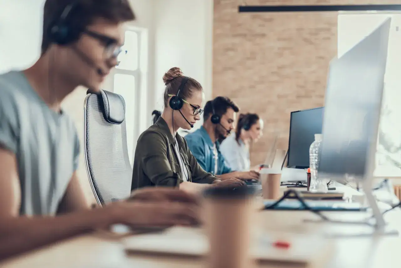 Personas trabajando en un centro de llamadas, similar a la diferencia entre funcionario y funcionario de carrera, todos concentrados en sus tareas.