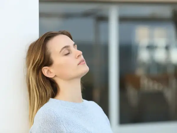 Mujer con ojos cerrados, apoyada en pared blanca, reflexionando sobre cuanto se cobra estando de baja por ansiedad.