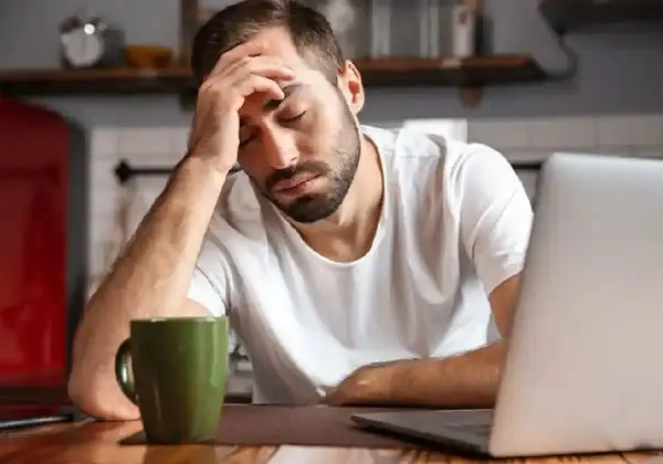 Hombre con dolor de cabeza frente a un portátil, con una taza verde. Necesita un justificante médico Andalucía.