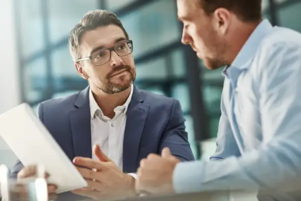 Un consultor de RRHH con gafas explica algo en una tablet a un colega.