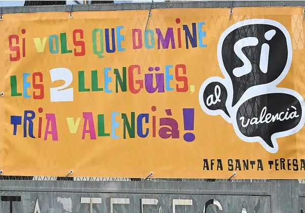 Cartel naranja con letras de colores: "Si vols que domines les llengües, tria València!". Promociona cursos homologados en València.