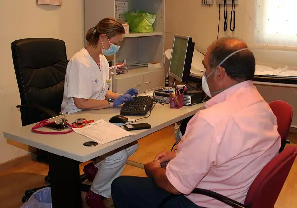 Enfermera con mascarilla atiende a paciente con mascarilla, tramitando un hospital justificante médico urgencias.