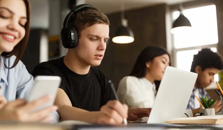 Estudiantes concentrados, uno con auriculares y portátil, aprendiendo cómo homologar un curso privado.