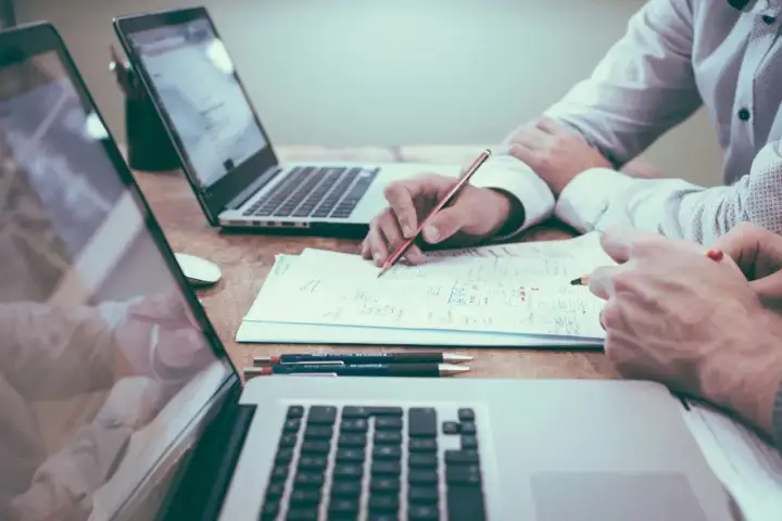 Dos personas analizan documentos y planifican, quizás sobre una nomina retribucion flexible. Laptops y bolígrafos a la vista.